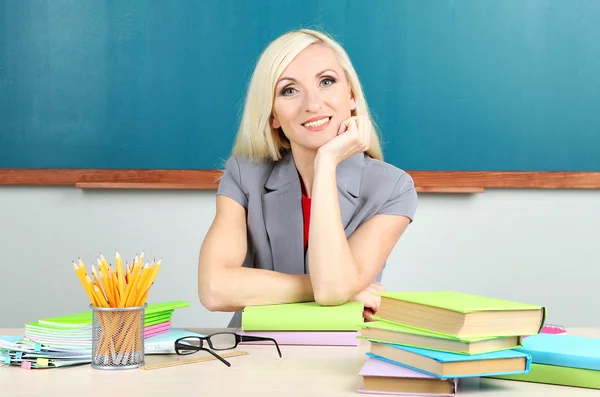 Schoolleraar zittend aan tafel op blackboard achtergrond — Stockfoto