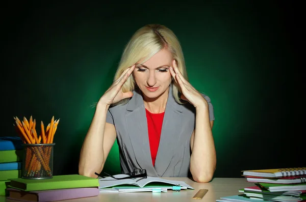 Unavený učitel sedí u stolu na tmavé barevné pozadí — Stock fotografie
