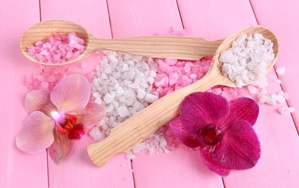 Still life with beautiful blooming orchid flower and wooden spoons with sea salt, on color wooden background — Stock Photo, Image