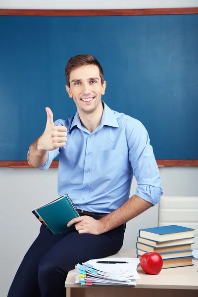 Joven profesor sentado en el escritorio en el aula de la escuela — Foto de Stock