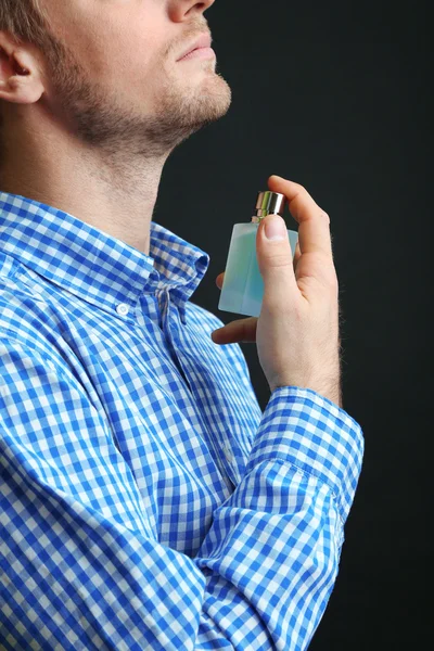 Pohledný mladý muž pomocí parfém na černém pozadí — Stock fotografie