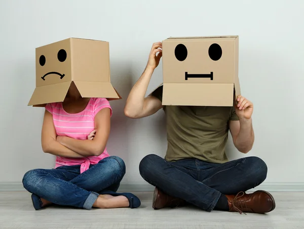 Couple with cardboard boxes on their heads sitting on floor near wall — Stock Photo, Image