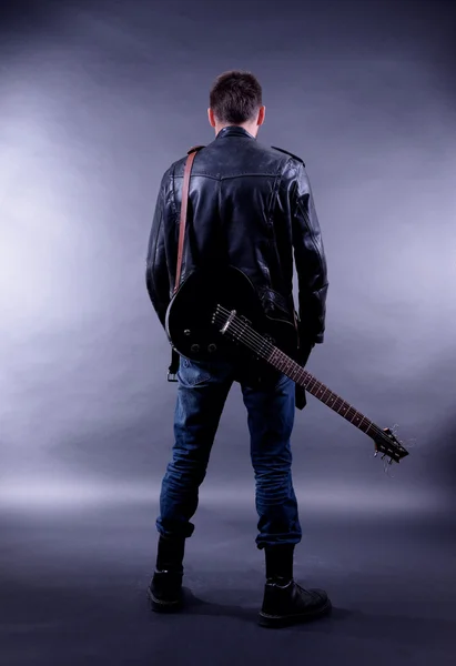 Joven músico con guitarra sobre fondo de color oscuro — Foto de Stock