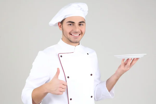 Chef profesional en uniforme blanco y sombrero, sobre fondo gris — Foto de Stock