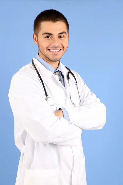 Médico masculino de pé com pasta, no fundo azul — Fotografia de Stock