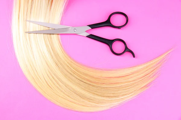 Lang blond haar met een schaar op roze achtergrond — Stockfoto