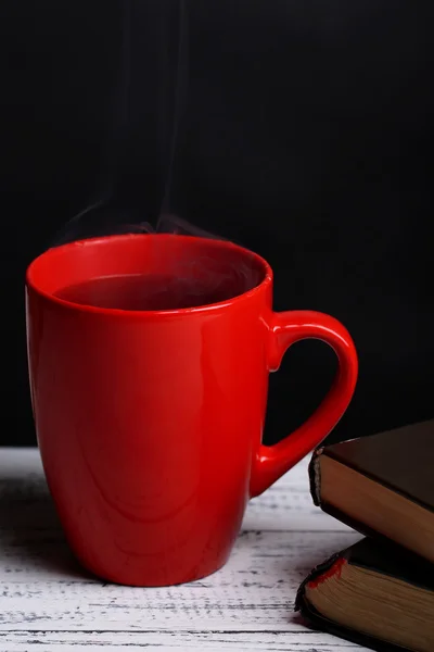 Чашка горячего чая с книгами на столе на темном фоне — стоковое фото