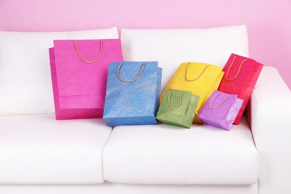 Colorful shopping bags on sofa, on color wall background — Stock Photo, Image