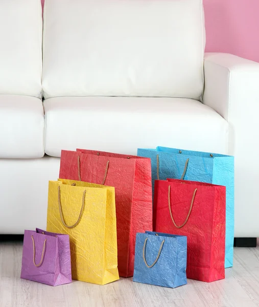 Divan, renkli duvar arka plan üzerinde renkli alışveriş torbaları — Stok fotoğraf