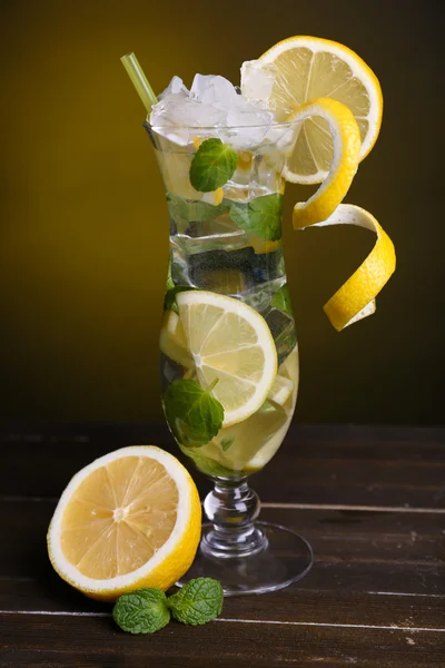 Glass of cocktail with lemon and mint on table on dark yellow background — Stock Photo, Image