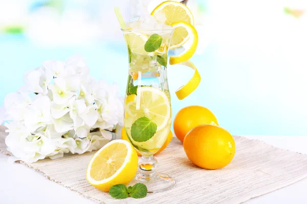 Glass of cocktail with lemon and mint on table on light blue background — Stock Photo, Image