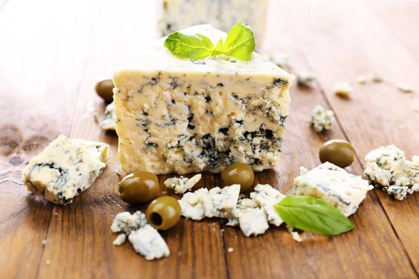 Smakelijke blauwe kaas met olijven en basilicum, op houten tafel — Stockfoto