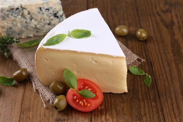 Tasty Camembert cheese with tomato, basil and olives, on wooden table — Stock Photo, Image