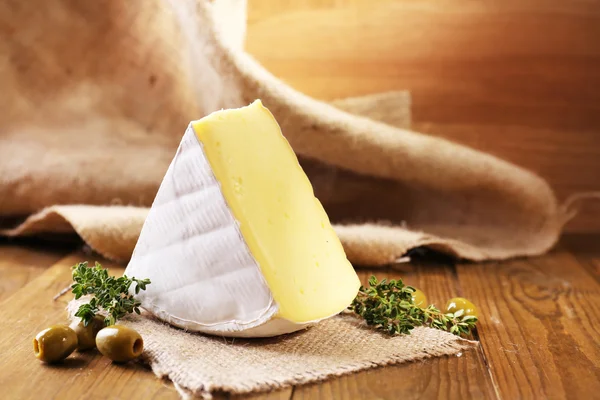 Tasty Camembert cheese with thyme and olives, on wooden table — Stock Photo, Image