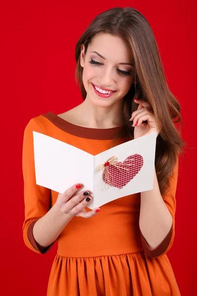 Attraktive Frau mit Postkarte, auf rotem Hintergrund — Stockfoto