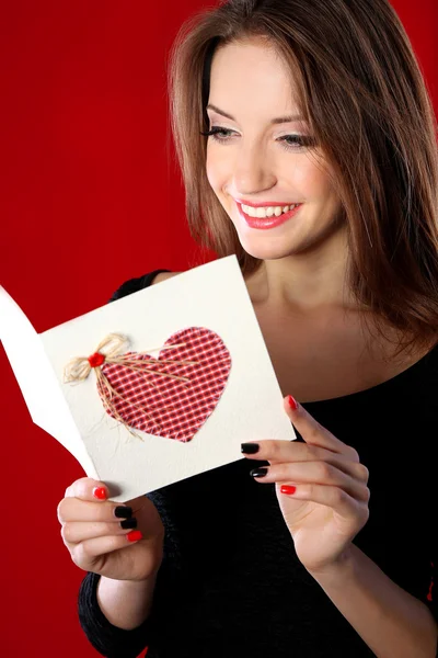 Attraktive Frau mit Postkarte, auf rotem Hintergrund — Stockfoto