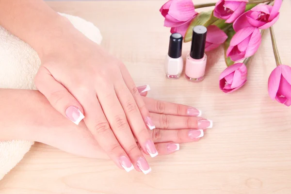 Hermosas manos de mujer con manicura francesa y flores sobre fondo de madera — Foto de Stock