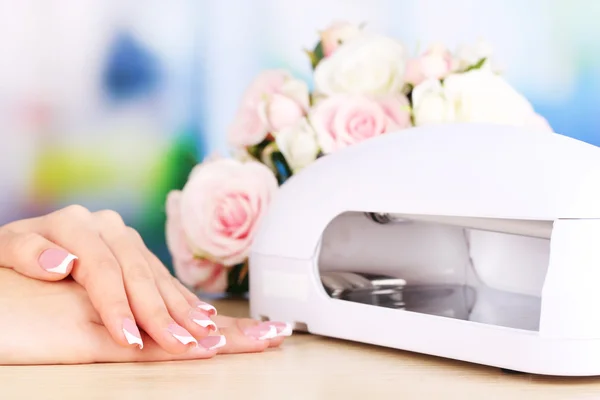 Mooie vrouw handen en lamp voor nagels op tabel op lichte achtergrond — Stockfoto