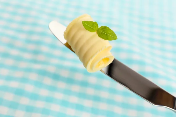 Curl of fresh butter with basil on knife on blue cloth — Stock Photo, Image