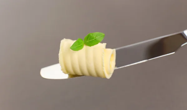 Rizo de mantequilla fresca con albahaca en el cuchillo sobre fondo gris —  Fotos de Stock