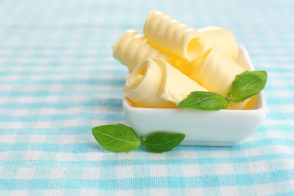 Curls of fresh butter with basil in bowl, on blue tablecloth — Stock Photo, Image