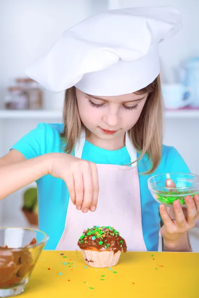 Liten flicka dekorera muffins i köket hemma — Stockfoto