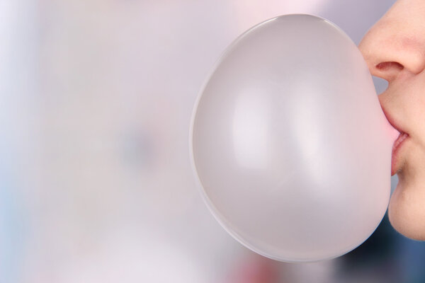 Person doing bubble with chewing gum on bright background