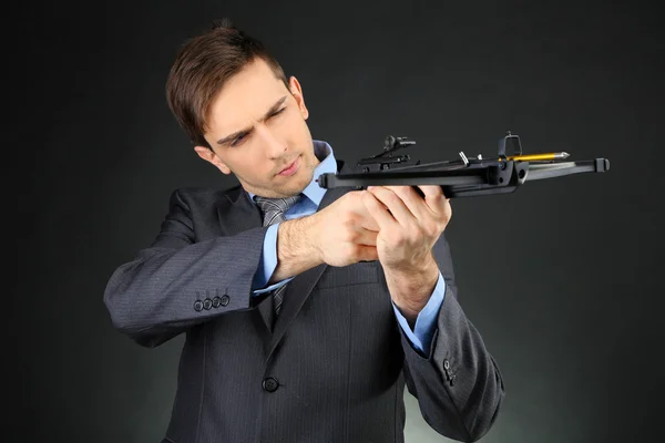 Young businessman with crossbow, on dark background — Stock Photo, Image