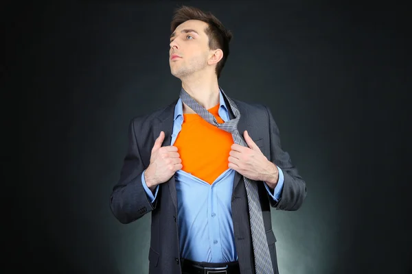 Jovem homem de negócios rasgando sua camisa revelando terno de super-herói, no fundo escuro — Fotografia de Stock