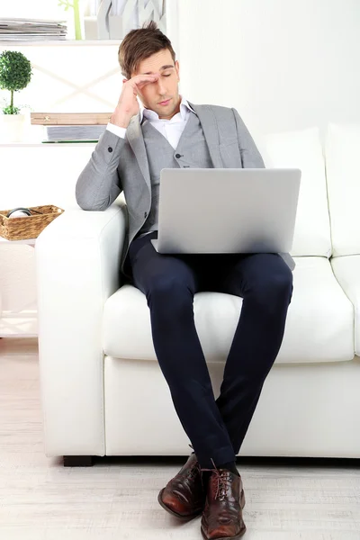 Молодой бизнесмен использует ноутбук на диване дома — стоковое фото