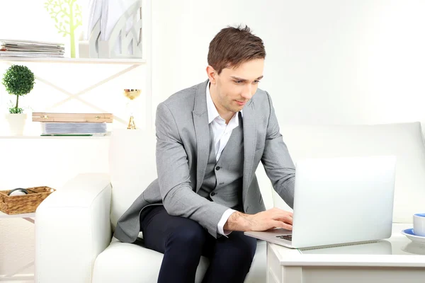 Jovem empresário sentado no sofá e usando laptop em casa — Fotografia de Stock