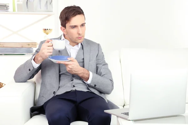 Elegante giovane uomo d'affari seduto sul divano e che beve caffè a casa — Foto Stock
