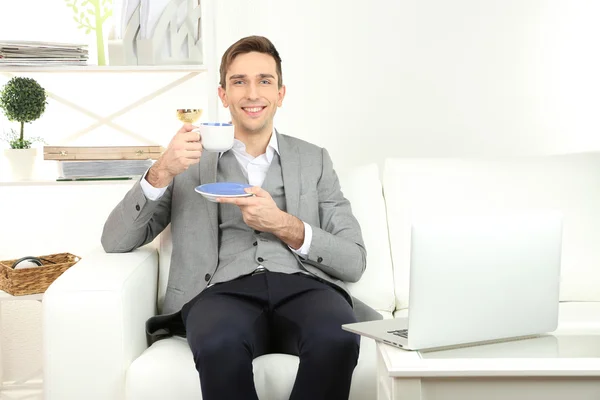 Eleganter junger Geschäftsmann sitzt auf dem Sofa und trinkt zu Hause Kaffee — Stockfoto