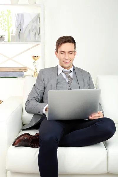 Ung affärsman sitter på soffan och använder bärbar dator hemma — Stockfoto