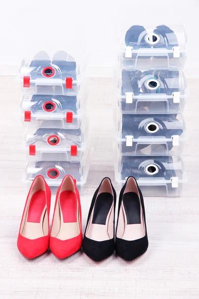 Boty v plastových bednách a ženské boty na podlaze v pokoji — Stock fotografie