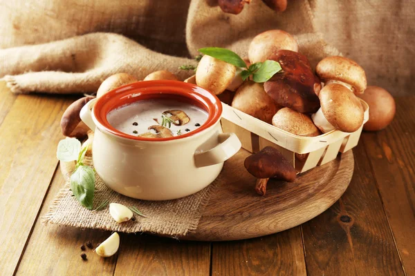Composition with mushroom soup in pot, fresh and dried mushrooms, on wooden table, on sackcloth background — Stock Photo, Image