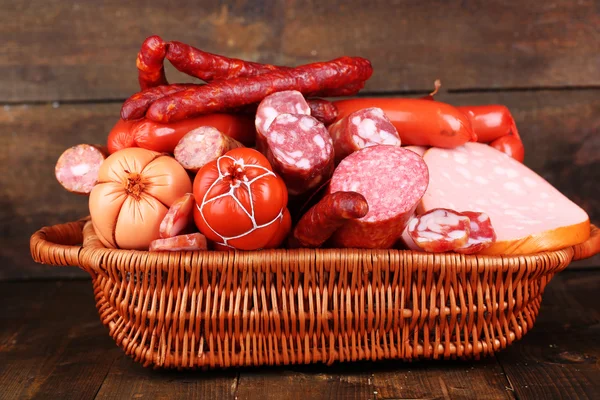 Lot of different sausages in basket on wooden table on wooden background — Stock Photo, Image