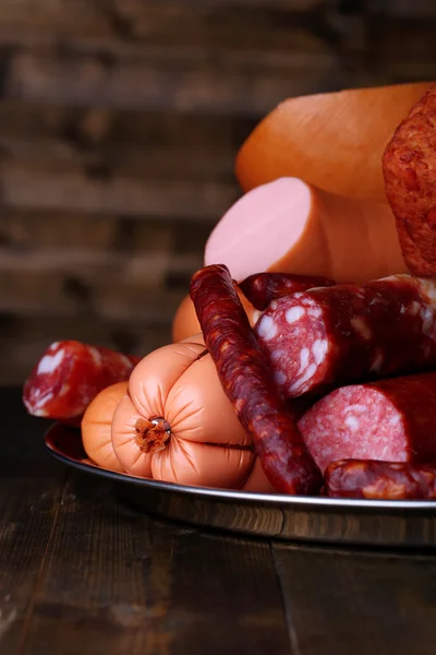 Lot of different sausages on salver on dark wooden background — Stock Photo, Image