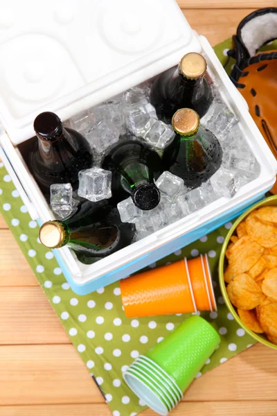 Ice chest full of drinks in bottles on color napkin, on wooden background — Stock Photo, Image