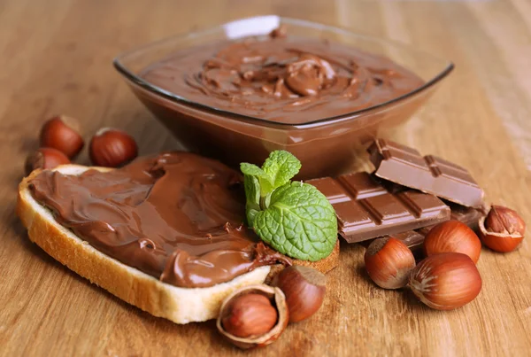 Pão com avelã de chocolate doce espalhado no fundo de madeira — Fotografia de Stock