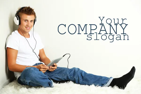 Jonge man ontspannen op tapijt en luisteren naar muziek, op grijze muur achtergrond — Stockfoto