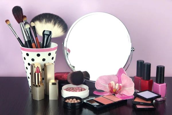 Espelho de mesa redonda com cosméticos e flor na mesa em fundo violeta — Fotografia de Stock