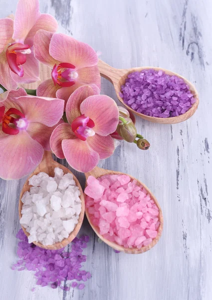 Still life with beautiful blooming orchid flower and wooden spoons with sea salt, on color wooden background — Stock Photo, Image