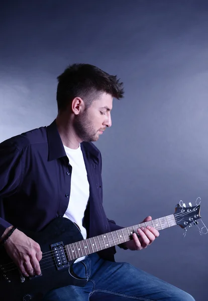 Joven músico tocando la guitarra sobre fondo gris —  Fotos de Stock