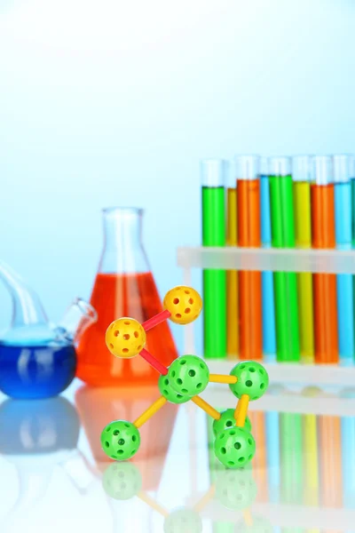 Modelo de molécula y tubos de ensayo con líquidos de colores sobre fondo azul — Foto de Stock