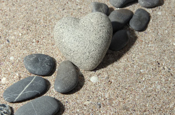 Grey stone in shape of heart, on sand background — Stock Photo, Image