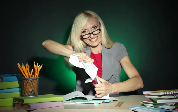 Böser Lehrer sitzt am Tisch auf dunklem, buntem Hintergrund — Stockfoto