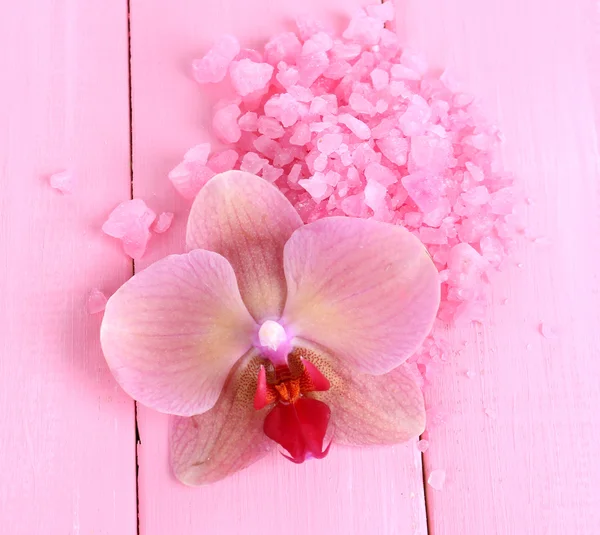 Beautiful blooming orchid flower and heap of sea salt, on color wooden background — Stock Photo, Image