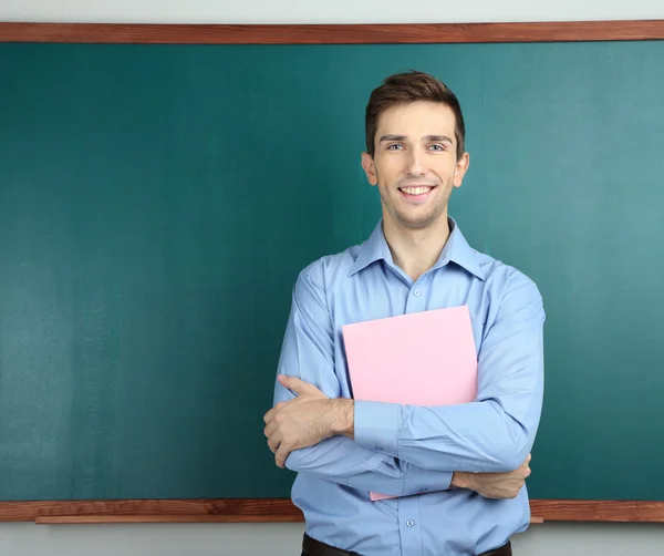 Νεαρός δάσκαλος με βιβλίο κοντά chalkboard σε σχολική τάξη — Φωτογραφία Αρχείου