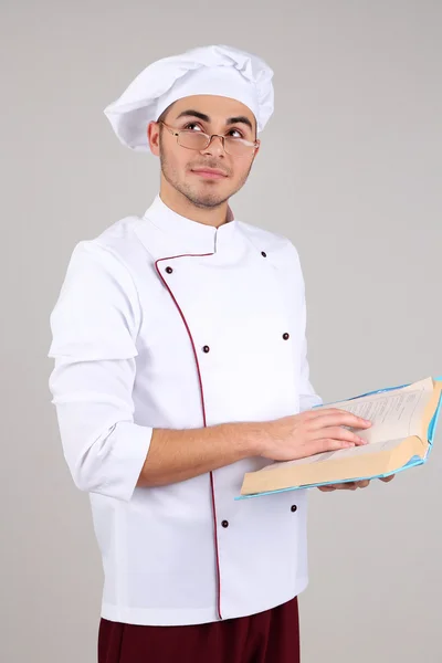 Profesjonalny kucharz w białej jednolite i kapelusz, prowadzące księgę, na szarym tle — Zdjęcie stockowe